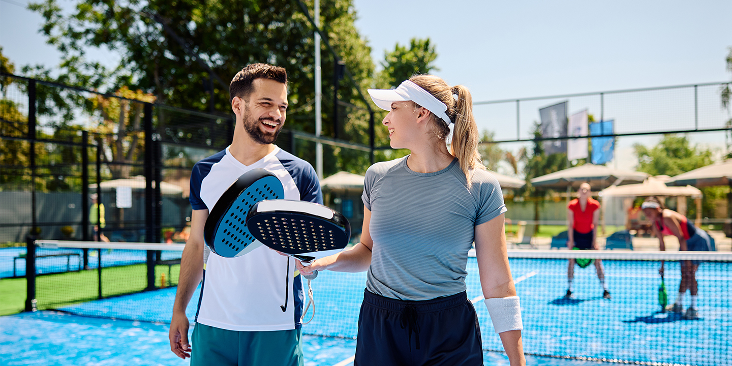 Happy paddle tennis players communicating during a match on an outdoor court.