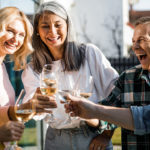 Smiling friends making toast during sunny day